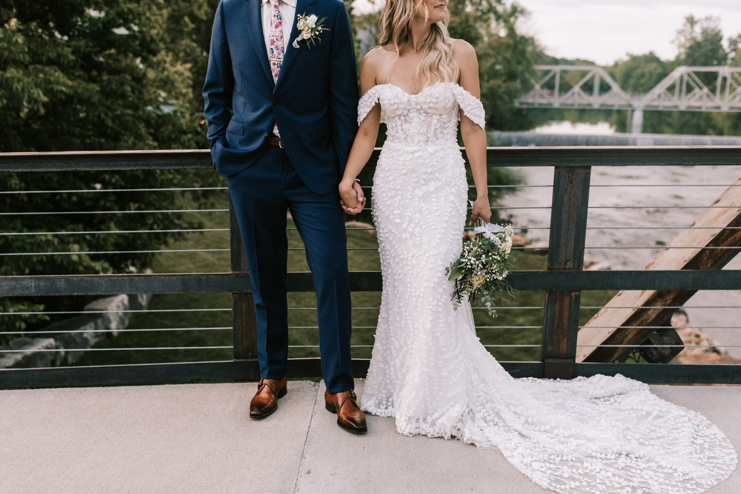 Bride and groom hold hands on the bridge at Finley Farms overlooking the Finley River.