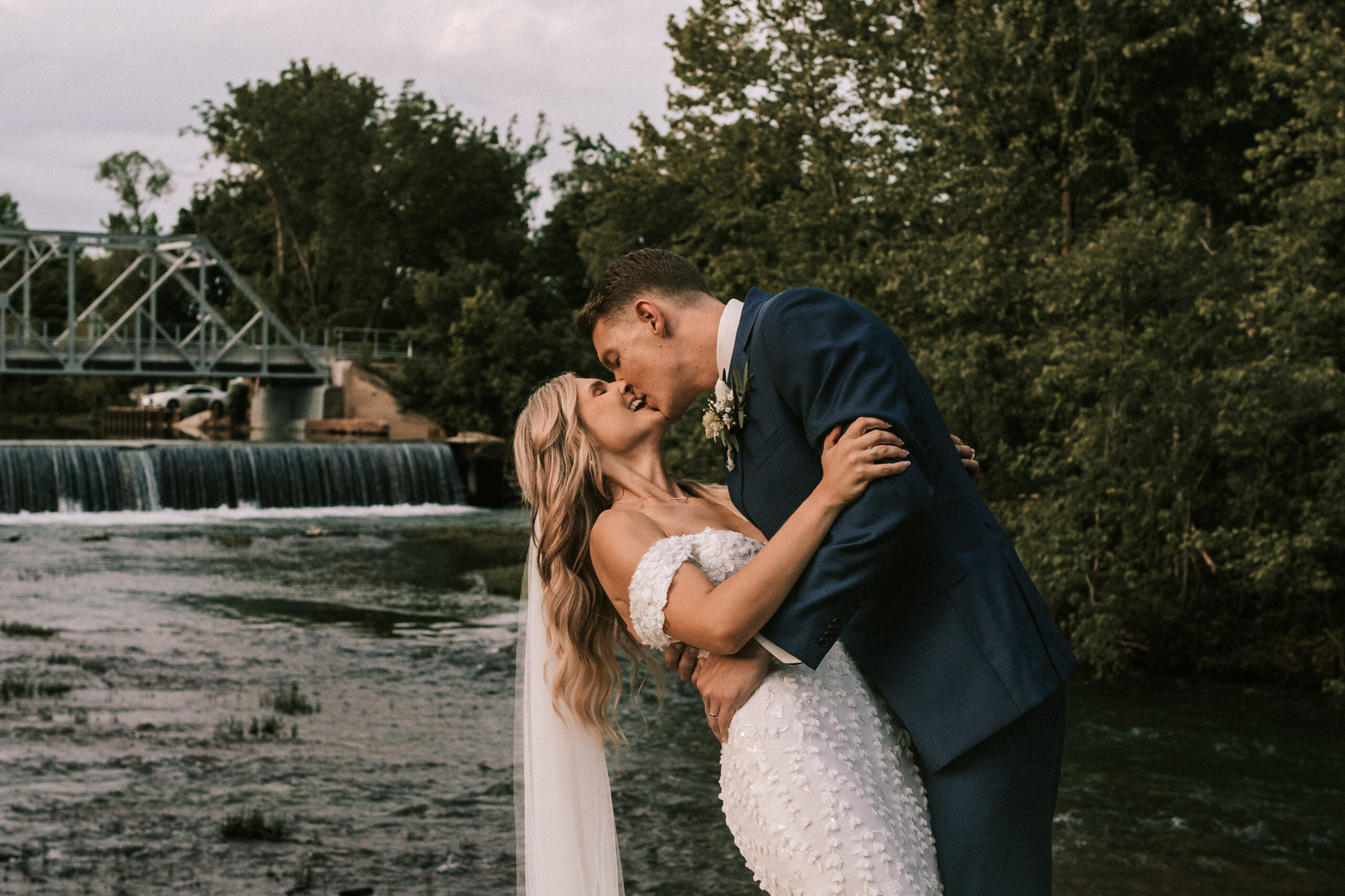 Groom dips his bride for a kiss in front of the Finley River.